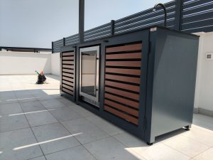 Vanjski hladnjak sa staklenim vratima ugrađen u tamnu aluminijsku kuhinju s drvenim panelima na otvorenoj terasi.