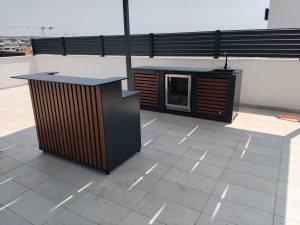 Ugradbeni vanjski hladnjak sa staklenim vratima u aluminijskoj kuhinji s drvenim letvicama na prostranoj terasi.